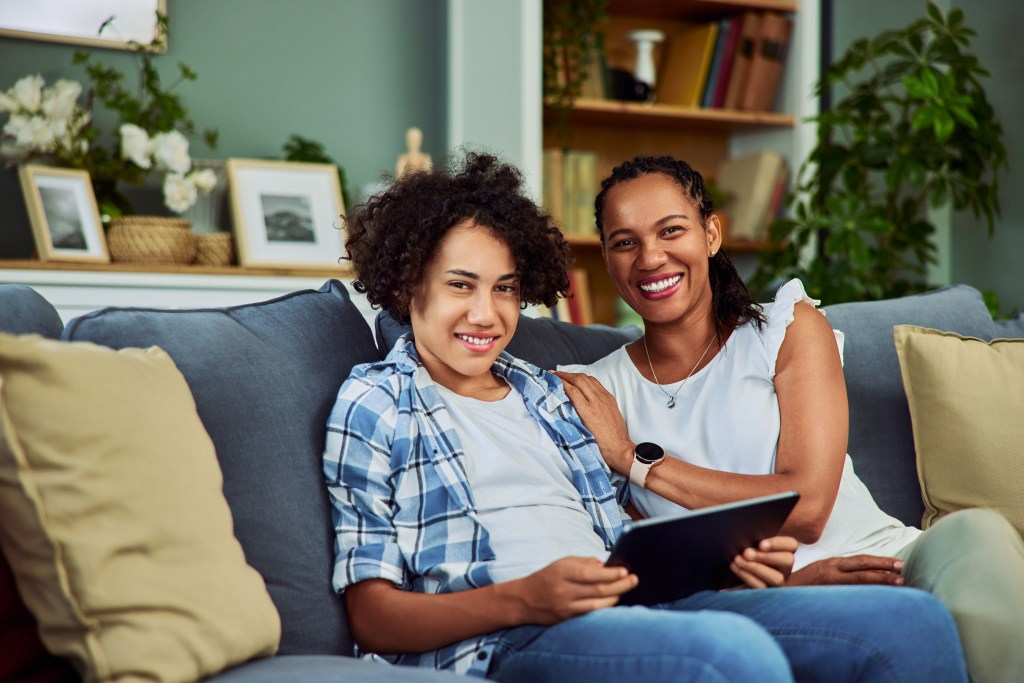 Happy African American mother and son smiling at the camera while sitting on a sofa at home